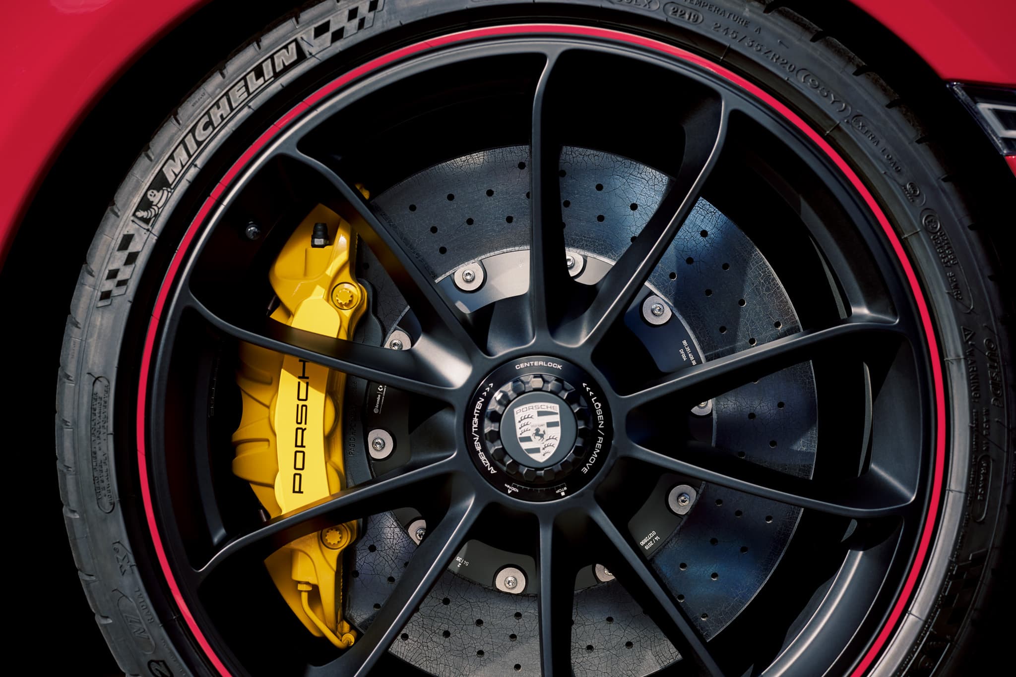 Close-up of a black alloy wheel with red trim, featuring a yellow Porsche brake caliper and Michelin N-Marked tire branding.